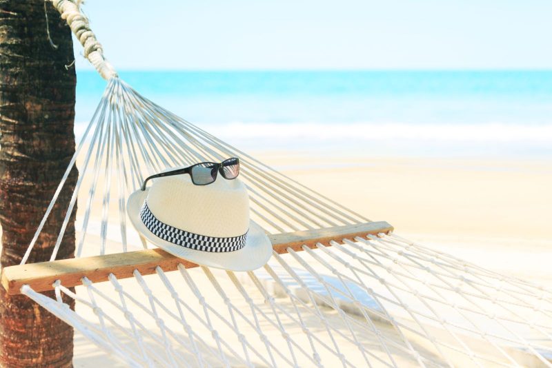 A hat and sunglasses sit on a hammock on a beach